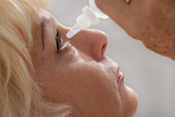 bolezen suhih oči in hormoni pri starejši ženski na sliki, ki si daje kapljice